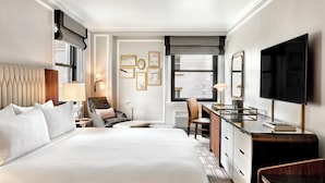 A hotel room with a large bed, a desk, a chair, a TV, and artwork on the wall. - Omni Parker House  (Boston)