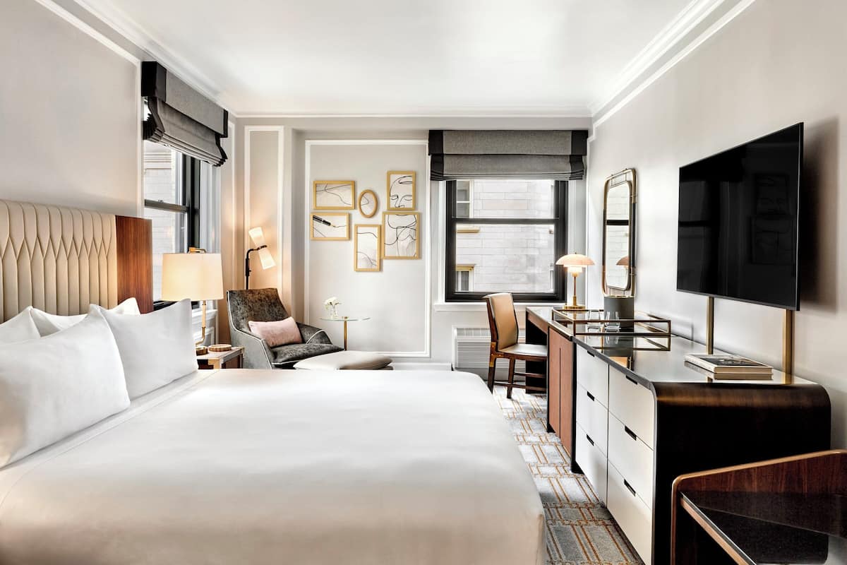Une chambre d’hôtel avec un grand lit, un bureau, une chaise, une télévision et des œuvres d’art accrochées au mur.