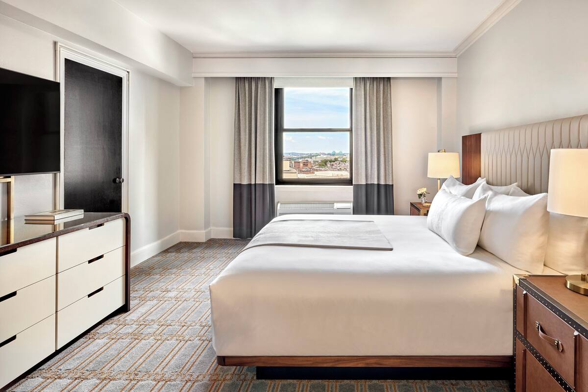 Une chambre d’hôtel avec un grand lit, un téléviseur à écran plat, un bureau et une fenêtre avec des rideaux.