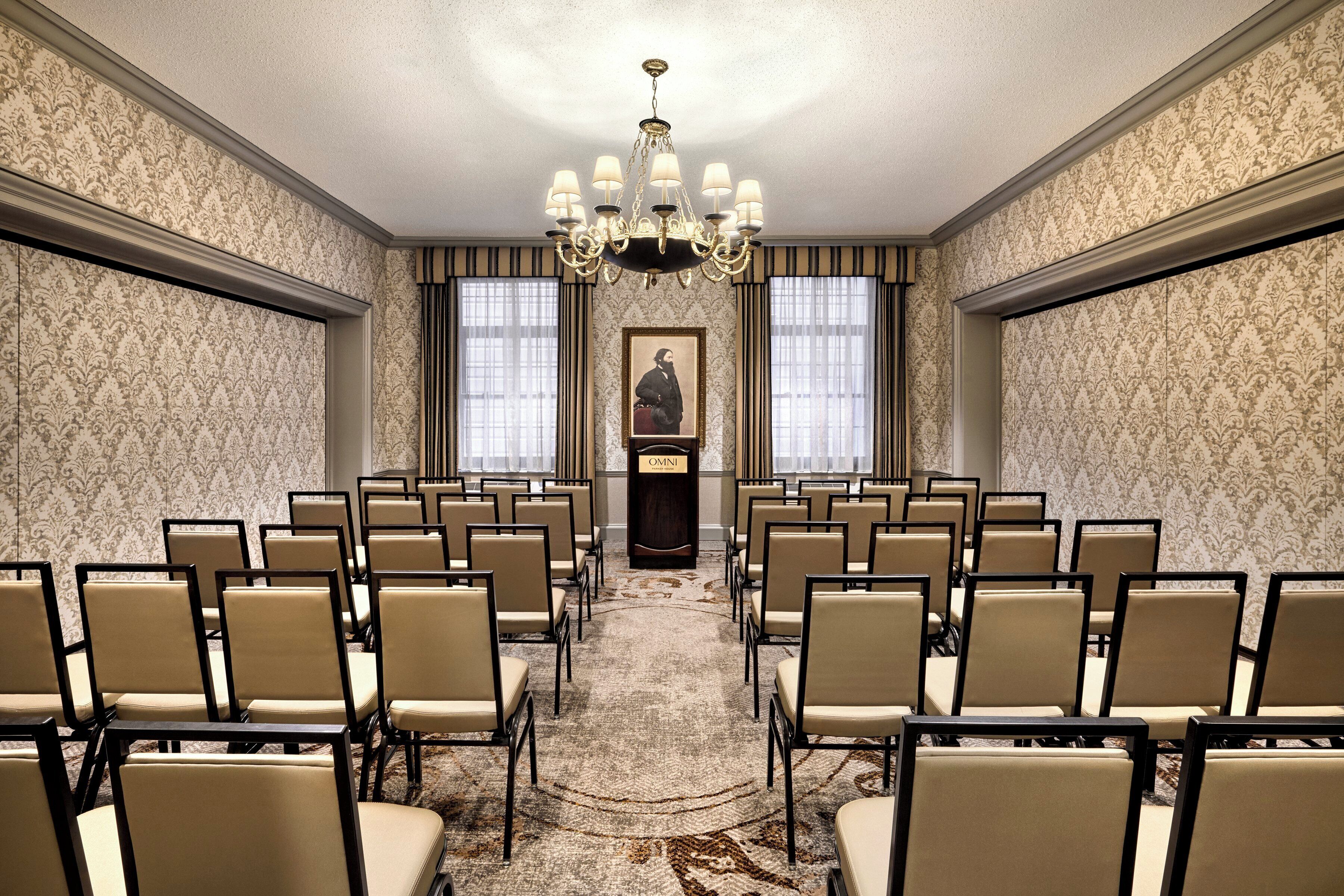 A conference room with rows of chairs, a chandelier, and a portrait on the wall.