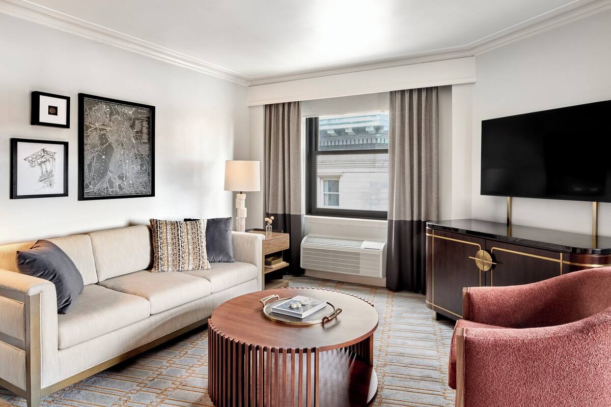 Une chambre d’hôtel moderne équipée d’un canapé, d’un fauteuil, d’une table basse ronde et d’un téléviseur à écran plat.