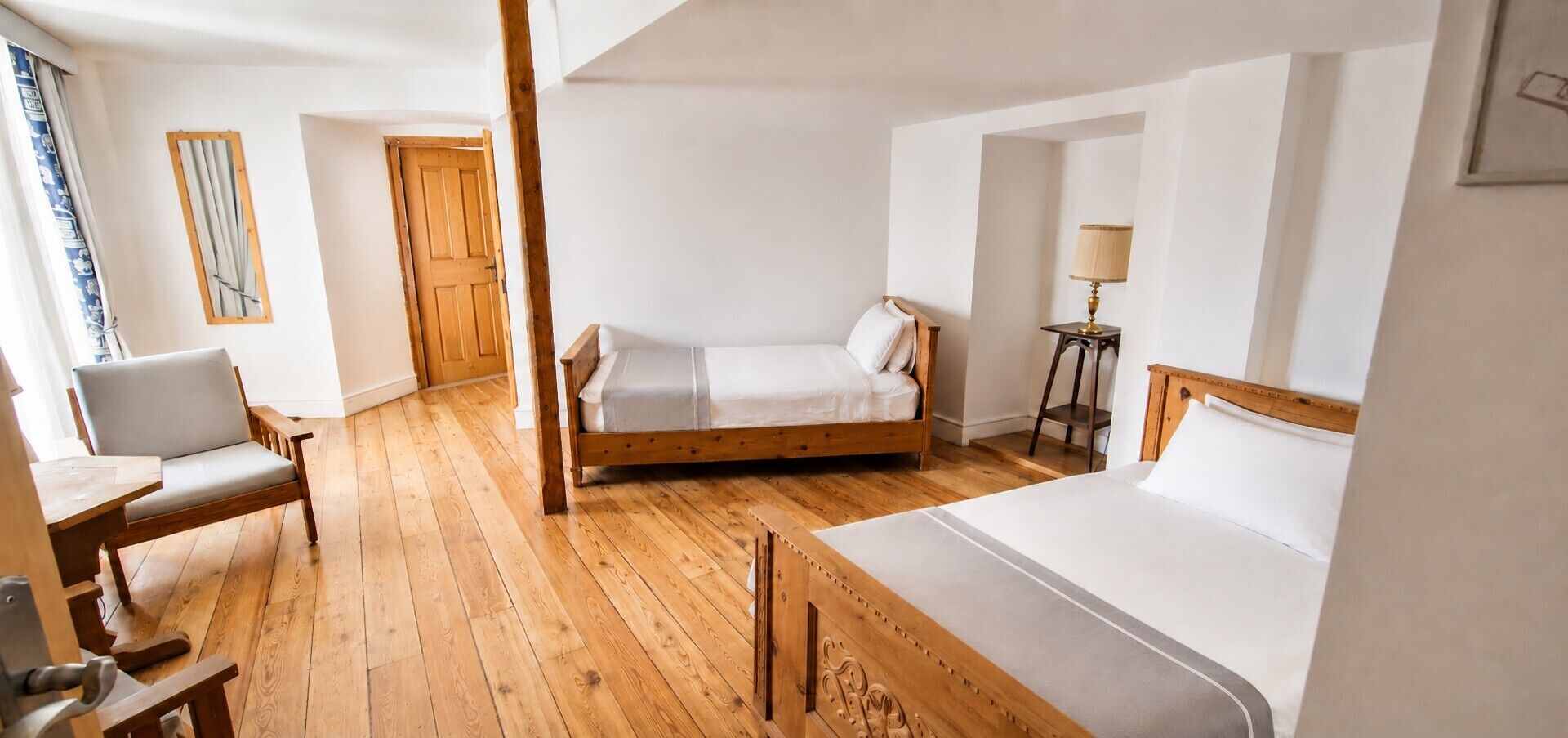 Ein Zimmer mit Holzboden, einem Bett, einem Stuhl, einem Schreibtisch und einer Lampe.