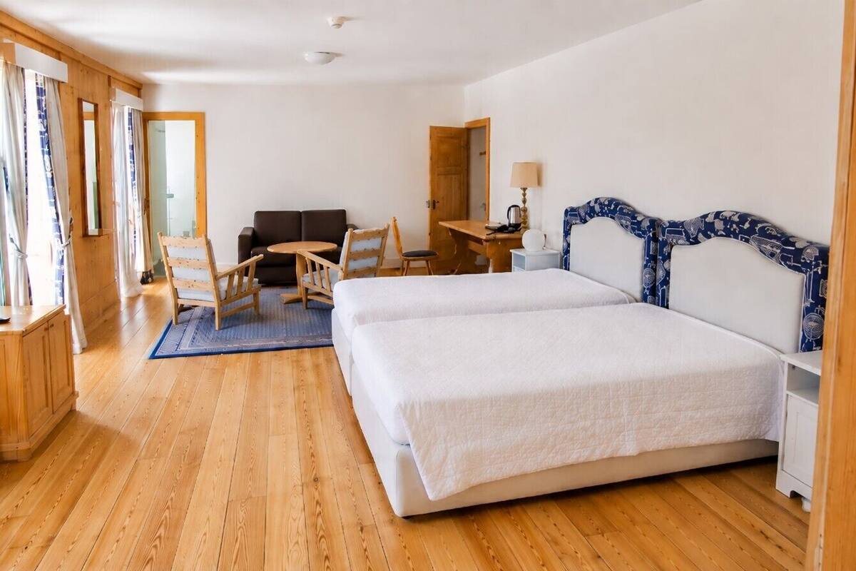 A room with two beds, a desk, a chair, and a window with curtains.