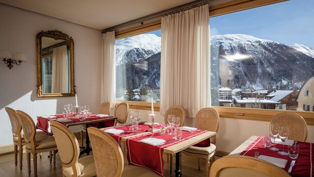 Un comedor con mesas dispuestas para cuatro personas, un espejo grande y vistas a montañas nevadas a través de la ventana.