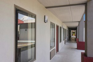 Um corredor com várias portas e janelas, que leva a um edifício com telhado vermelho.
