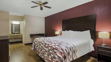 A hotel room with a bed, a nightstand, a desk, a chair, a ceiling fan, and a bathroom visible through an open door.