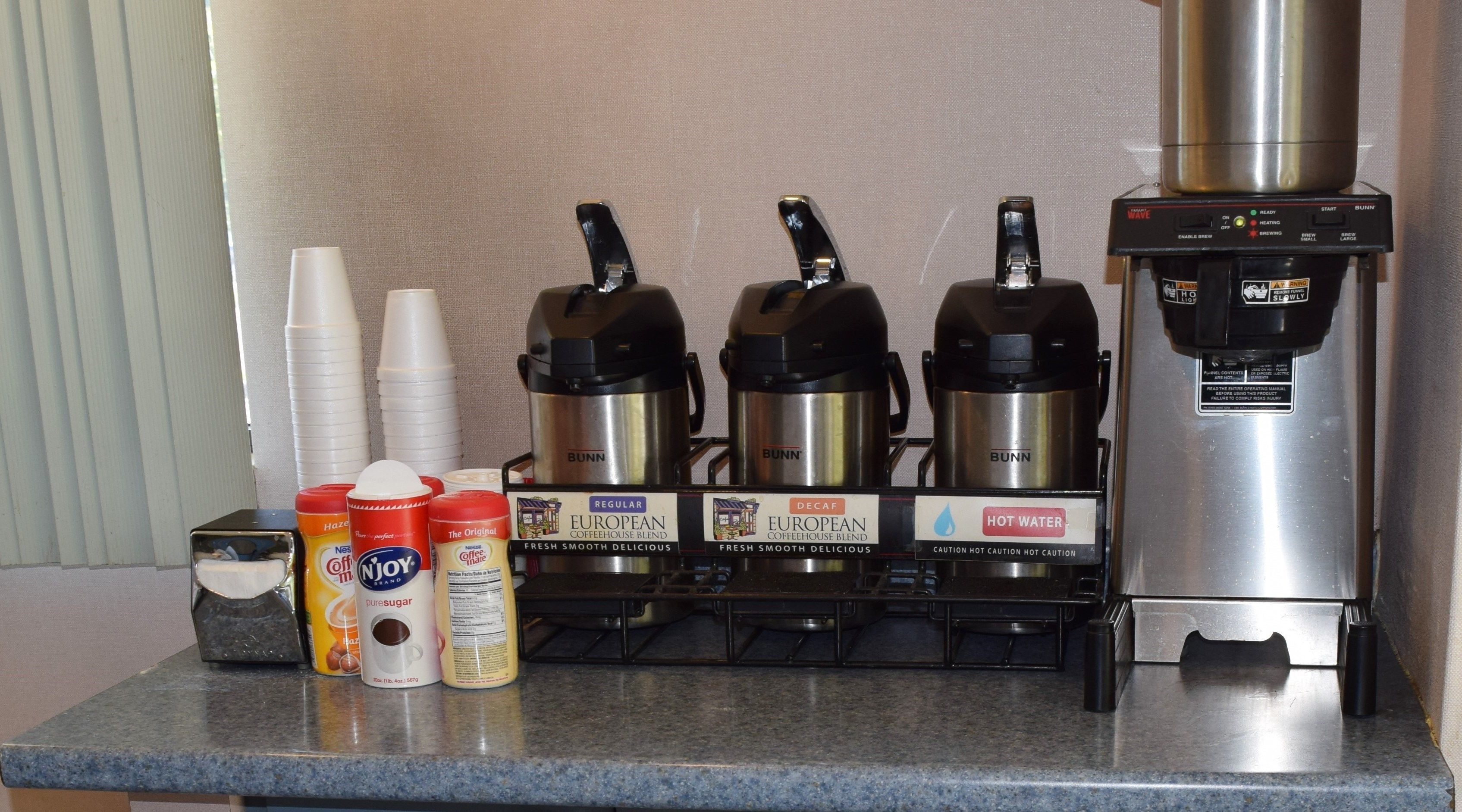 Una estación de café con tres máquinas de café, vasos desechables y diversas opciones de leche para café.