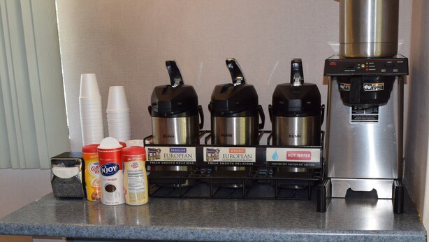 A coffee station with three coffee makers, disposable cups, and various coffee creamer options. - Red Roof Inn & Suites Statesboro - University (Statesboro)