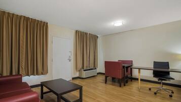 A hotel room with a wooden floor, a desk with a chair, a red sofa, and a door with curtains.