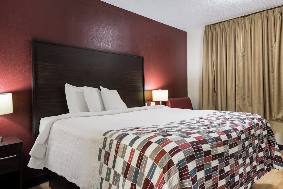 Een hotelkamer met een groot bed, twee nachtkastjes en een raam met gordijnen.