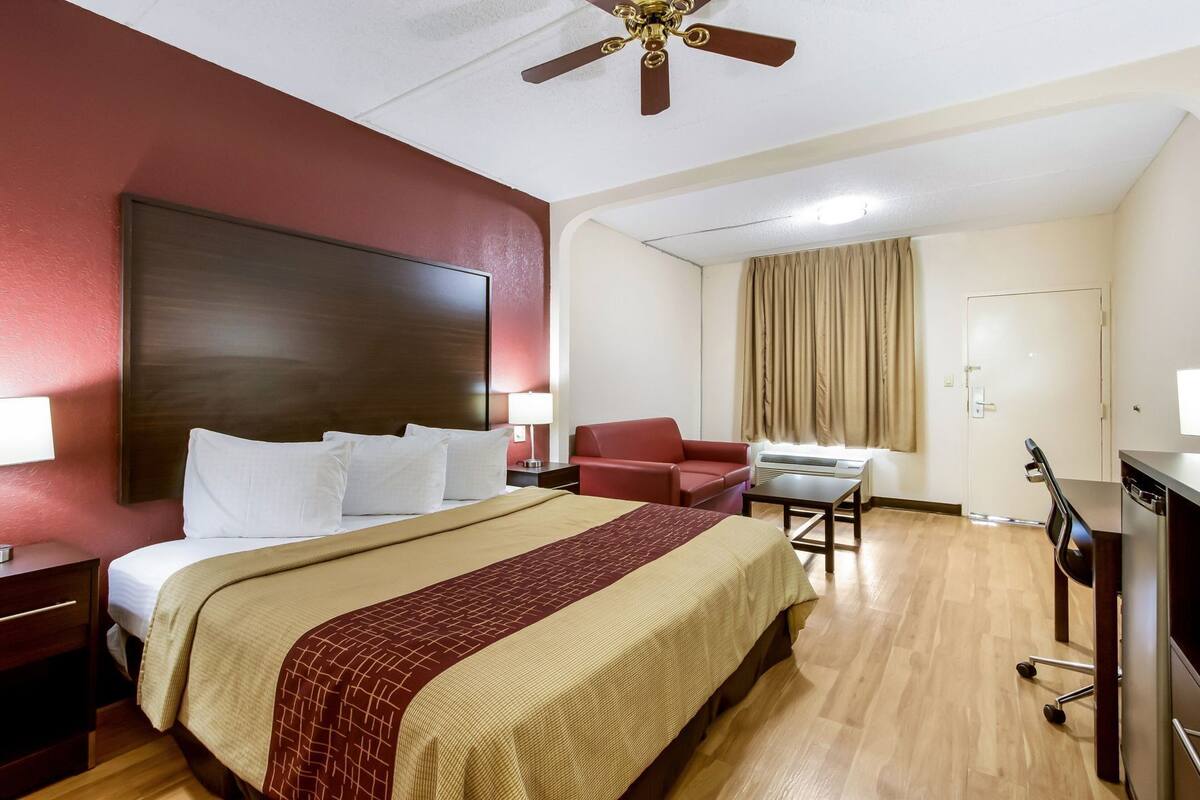 Een hotelkamer met een bed, een bureau, een stoel, een televisie, een plafondventilator en een deur.
