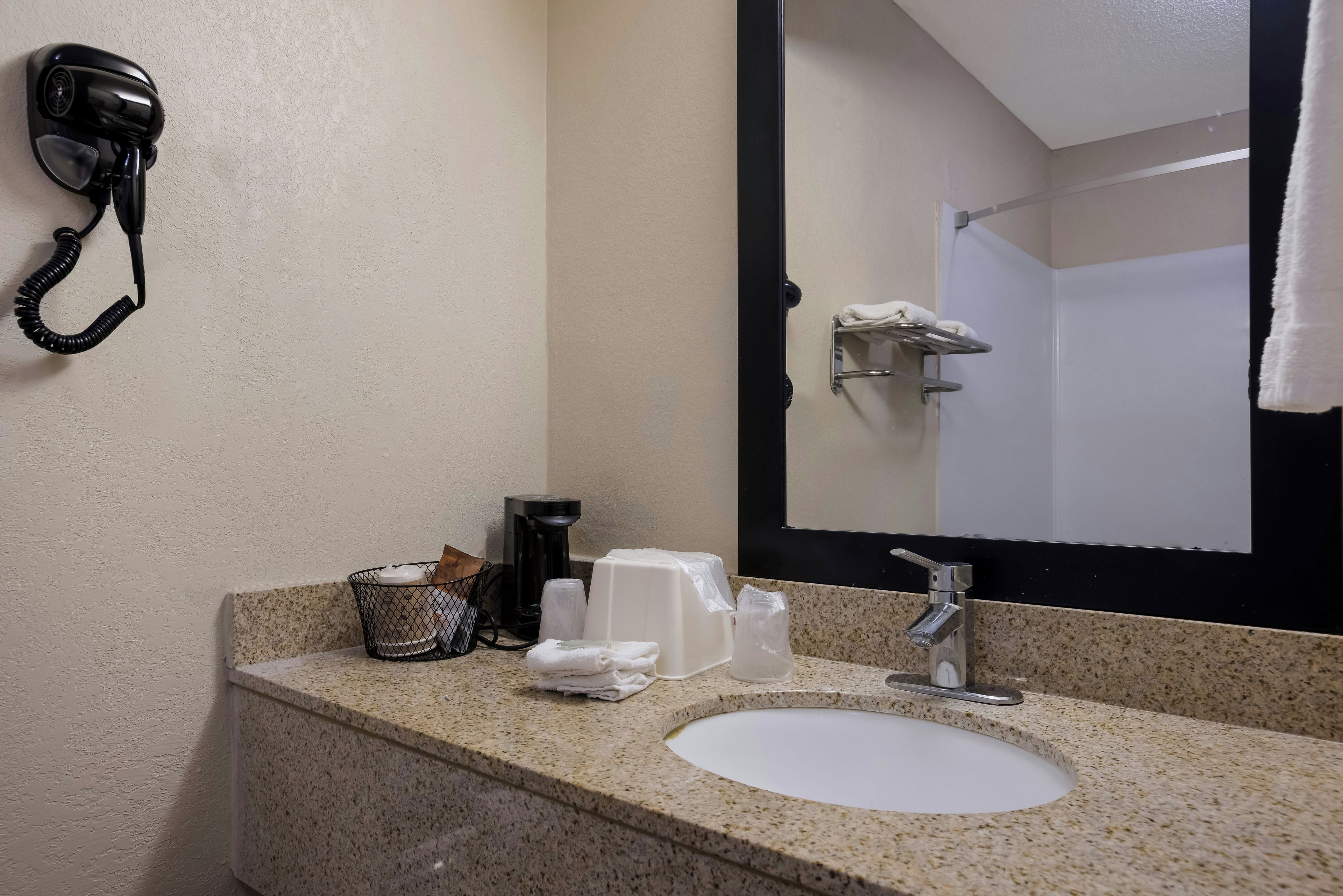 Ein Badezimmer in einem Hotel mit Waschbecken, Spiegel, Handtuchhalter und einem Föhn an der Wand.