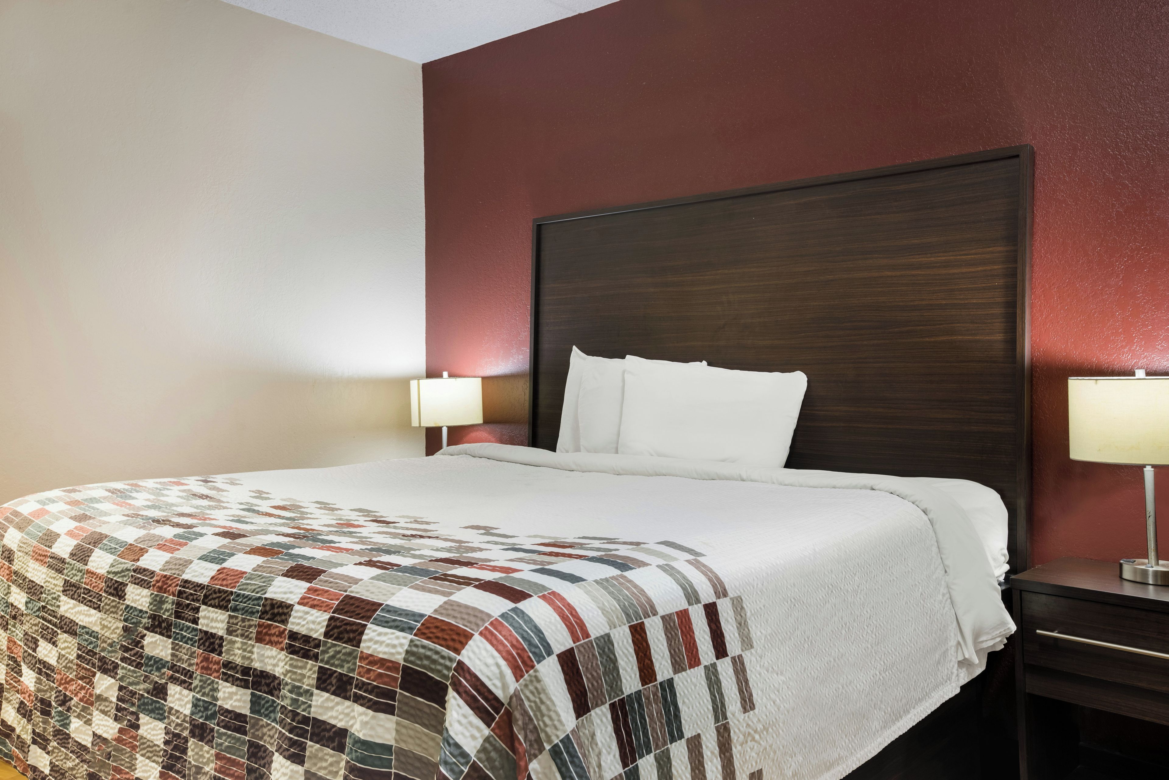 Una camera d'albergo con un letto grande, una testiera scura, due lampade ai comodini e una coperta trapuntata.
