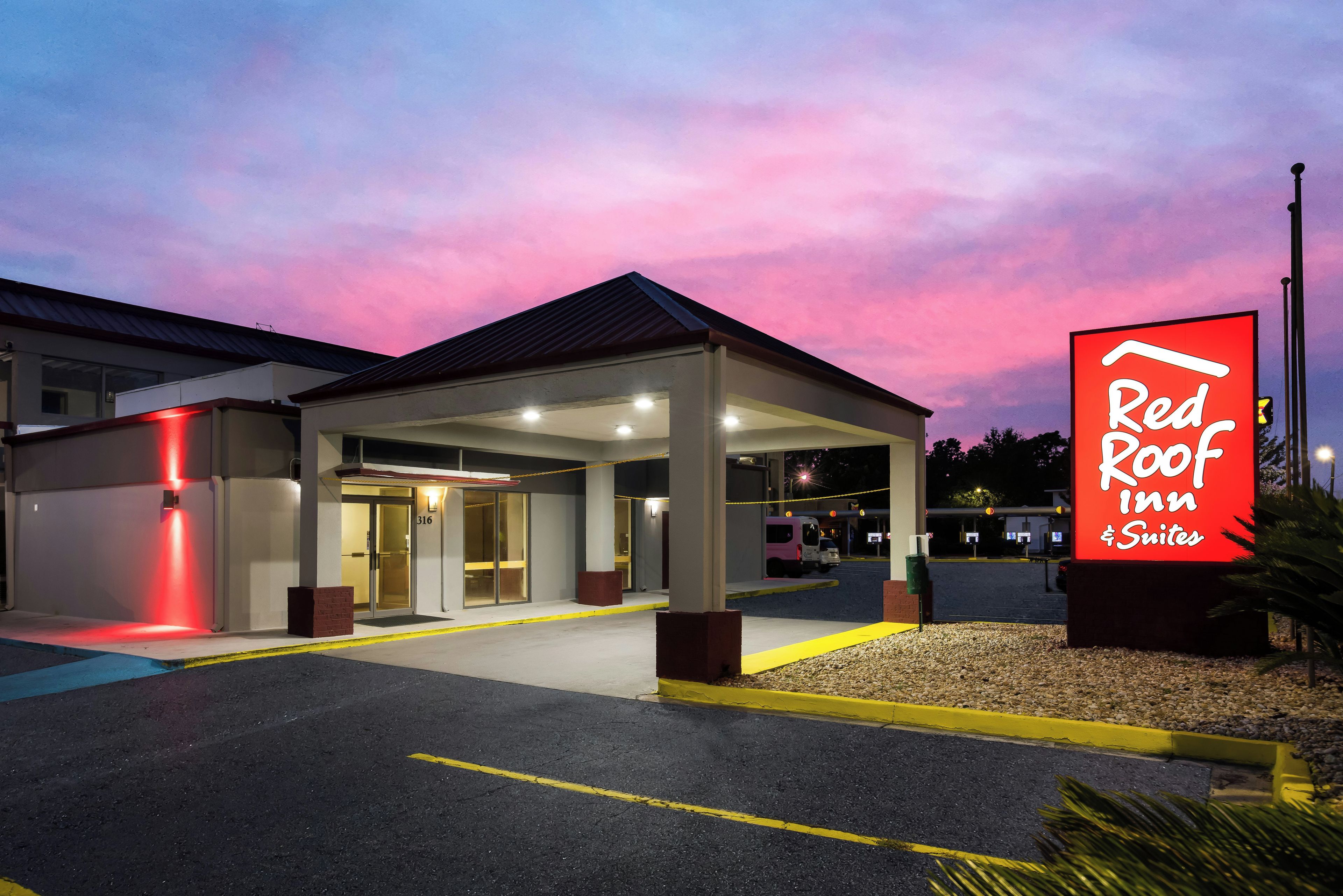 Een Red Roof Inn Suites met een overdekte ingang, een parkeerplaats en een heldere lucht.