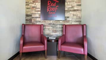 Two red leather chairs facing each other with a small table between them, a stone wall with a sign above, and a tiled floor.