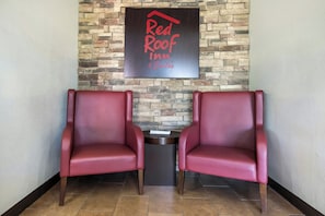 Two red leather chairs facing each other with a small table between them, a stone wall with a sign above, and a tiled floor.