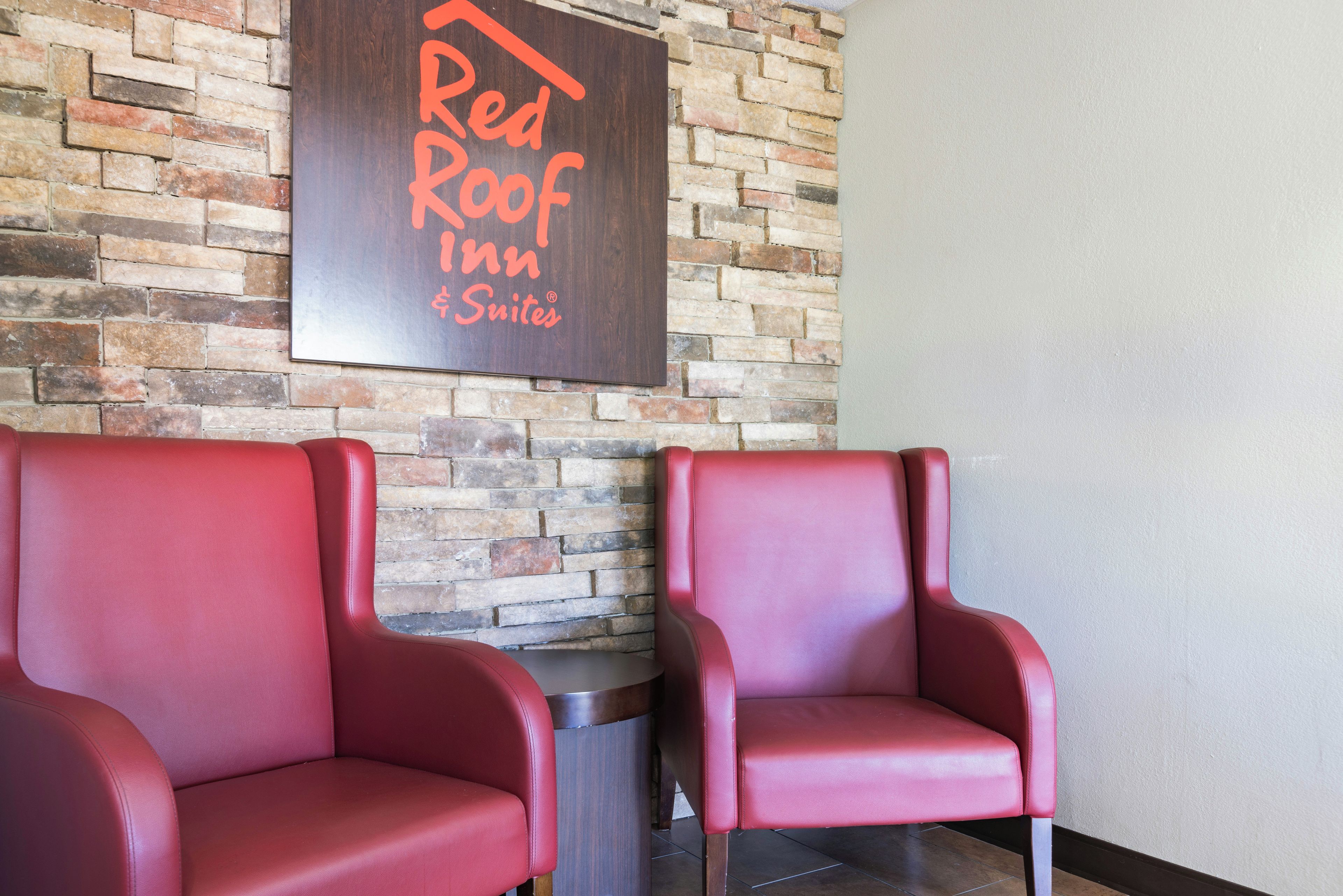 Deux fauteuils en cuir rouge se trouvent dans une pièce dont un mur est en briques et où est affiché un panneau indiquant « Red Roof Inn Suites ».