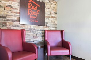 Twee rode leren stoelen in een kamer met een bakstenen muur en een bordje met de tekst 'Red Roof Inn Suites'.
