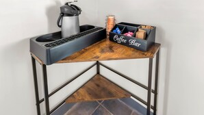 A corner table with a coffee maker, a mug, and a coffee bar storage box.