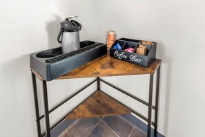 A corner table with a coffee maker, a mug, and a coffee bar storage box.