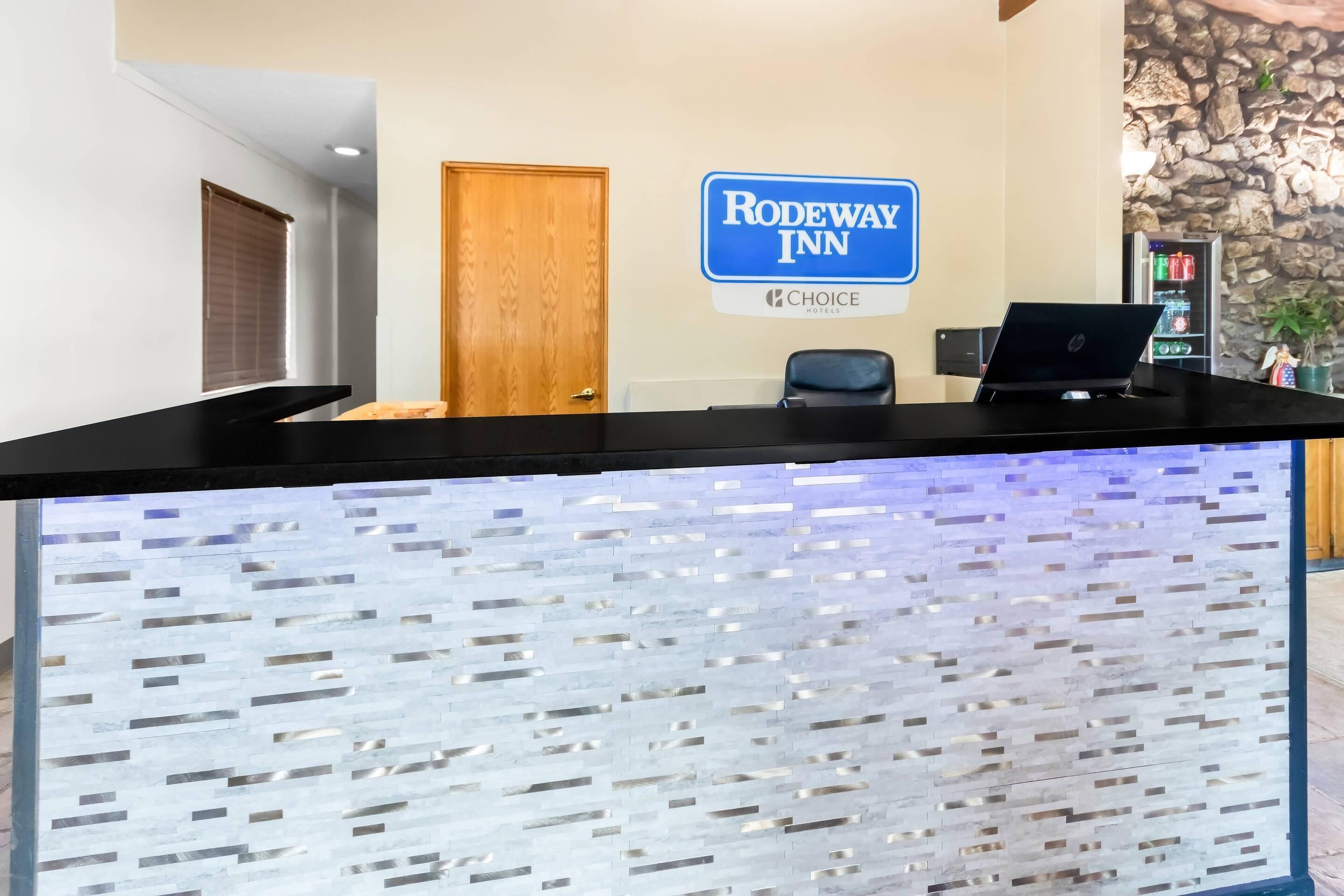 Una recepción con una computadora portátil, un letrero de Rodeway Inn y una pared de piedra.