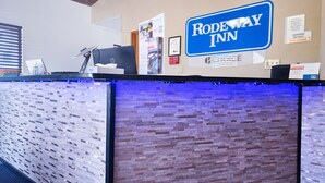 A reception desk with a sign reading "RODEWAY INN" and various informational posters and signs on the wall.