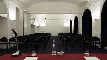 Une salle de conférence avec des rangées de chaises, un pupitre, une bouteille et des verres sur une table.