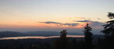 A panoramic view of a lake surrounded by hills and trees during sunset.