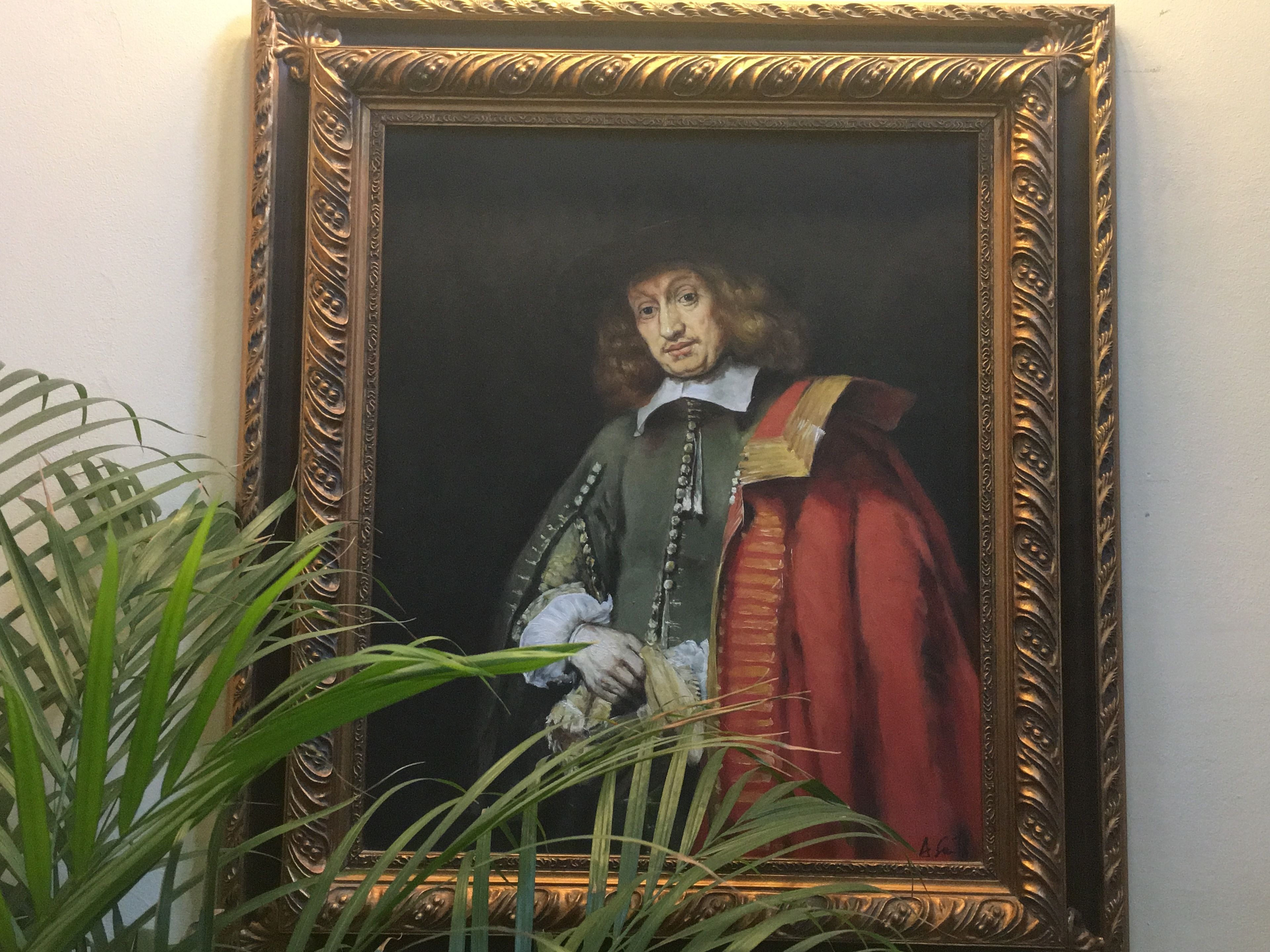 Un portrait encadré dans un cadre doré orné, représentant une personne vêtue d’une robe verte et rouge, et portant un col blanc.