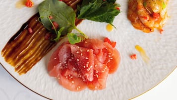 Une assiette blanche contenant divers aliments, notamment du saumon et des crevettes, décorée d’herbes aromatiques et de citron.