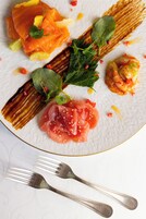 A white plate with various food items, including salmon and shrimp, garnished with herbs and lemon.