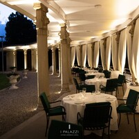 Un restaurante con mesas redondas y sillas verdes, ubicado en un espacio al aire libre con columnas y cortinas colgantes.