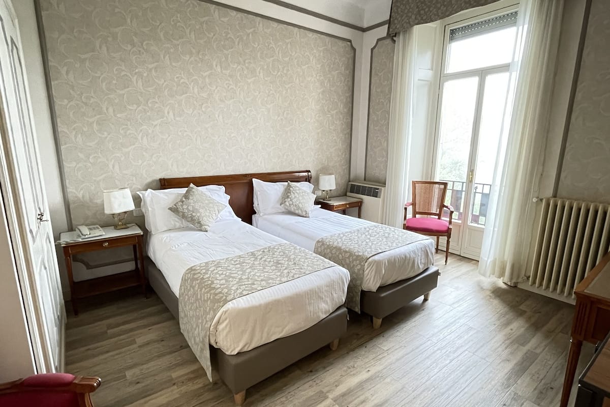 Une chambre d’hôtel avec deux lits, une chaise, une table de chevet avec une lampe et une fenêtre avec des rideaux.