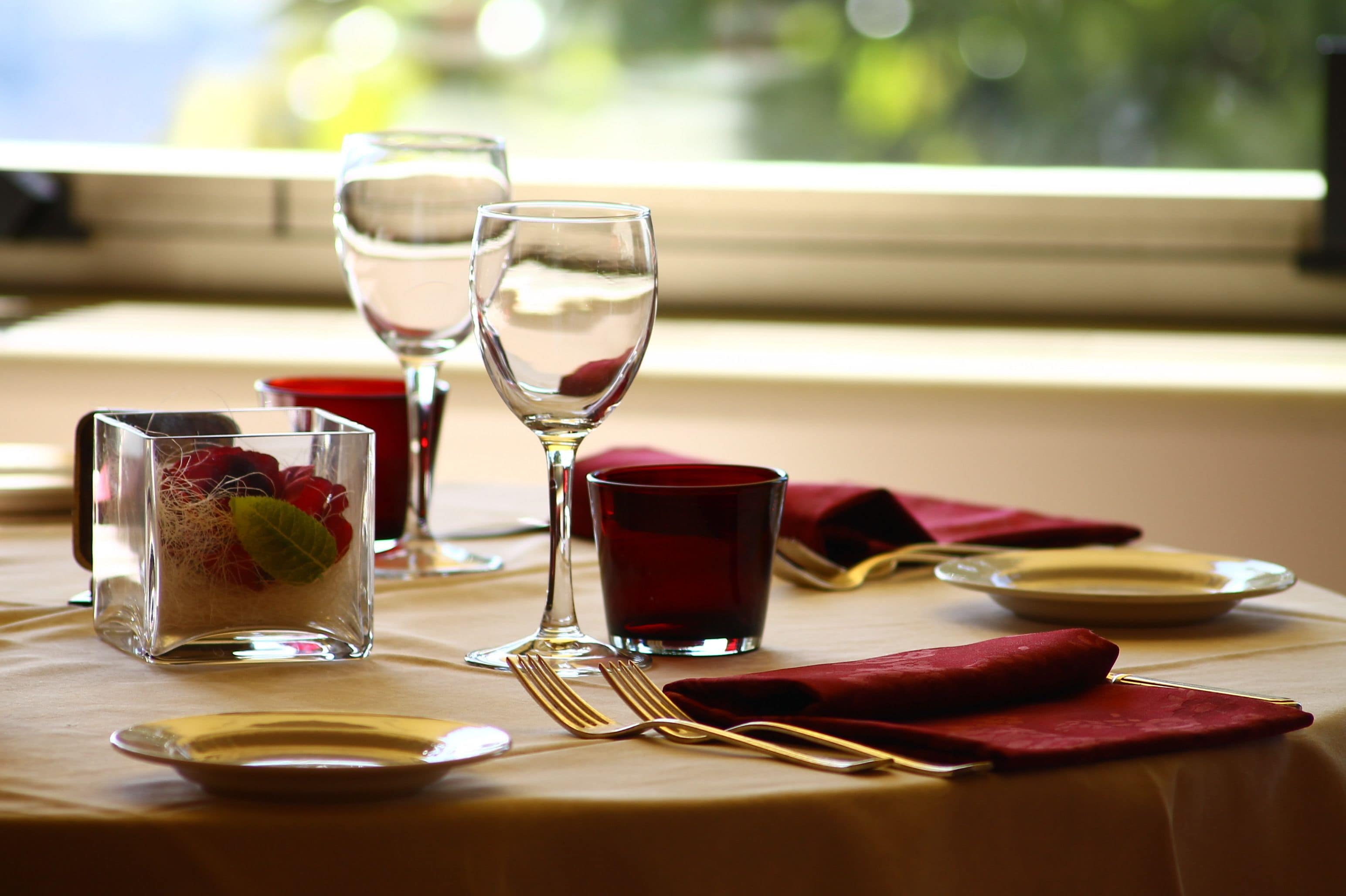 A table set for dining with clear glassware, a red napkin, and a glass of red beverage.