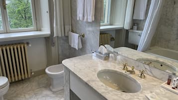 Ein Badezimmer mit Marmorwaschbecken, Toilette, Badewanne und einem Fenster mit Blick auf Bäume.
