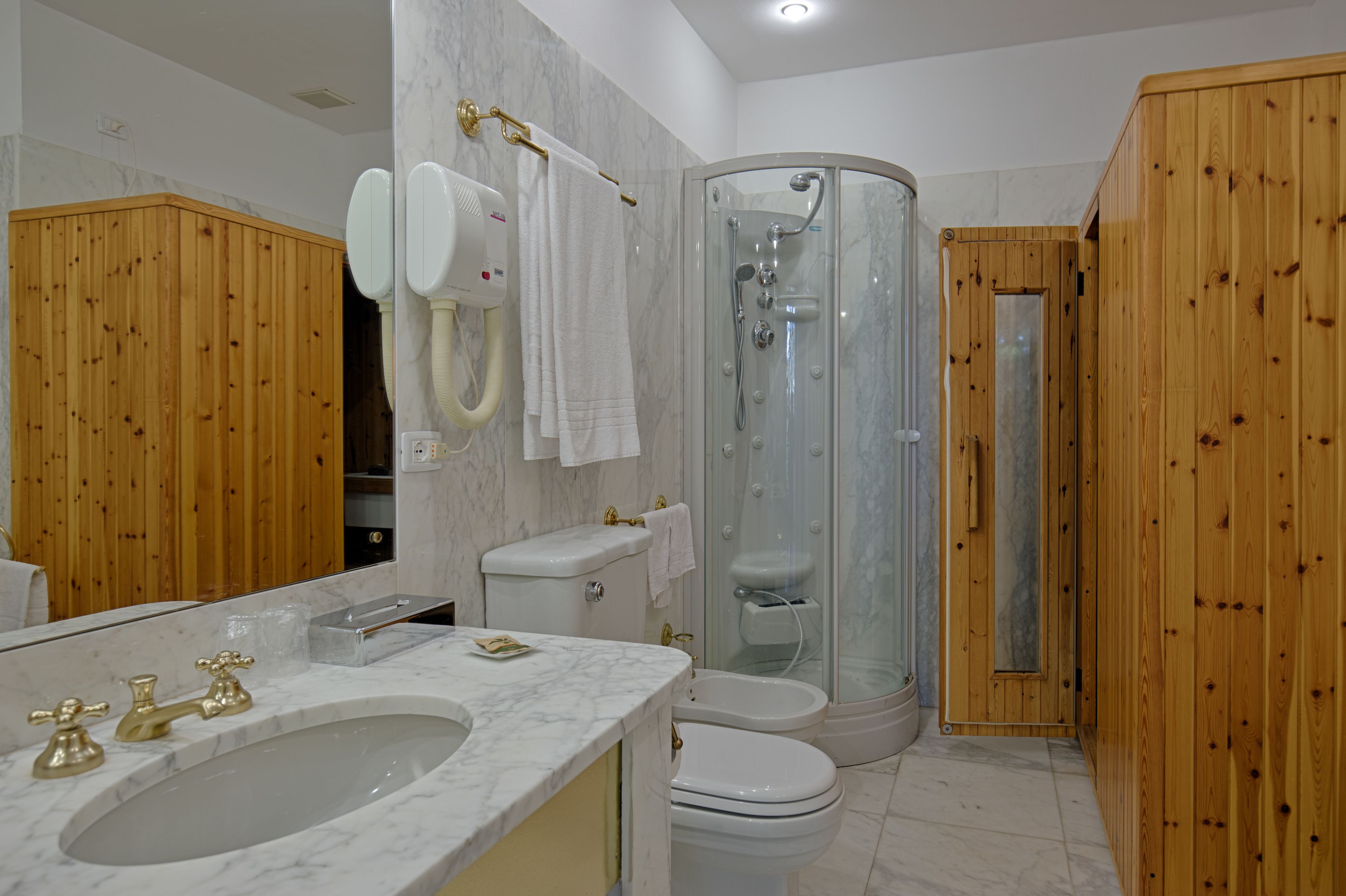 Ein Badezimmer mit Marmorwaschbecken, Toilette, Duschkabine und Holzvertäfelung.