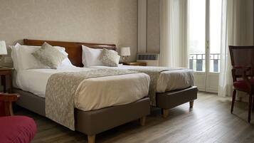A double bed with a wooden headboard, two bedside tables with lamps, a red chair, and a view of the outdoors through a large window.