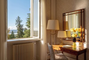 Una habitación con un ventanal grande, un escritorio con lámpara, un espejo y un florero con flores.