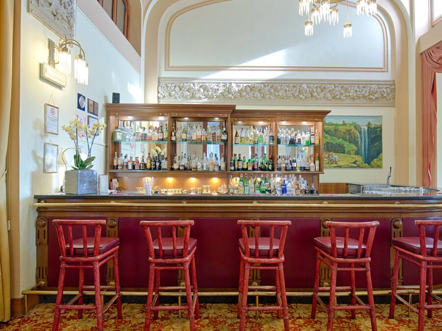 A bar area with a counter, multiple shelves of bottles, and four red bar stools.
