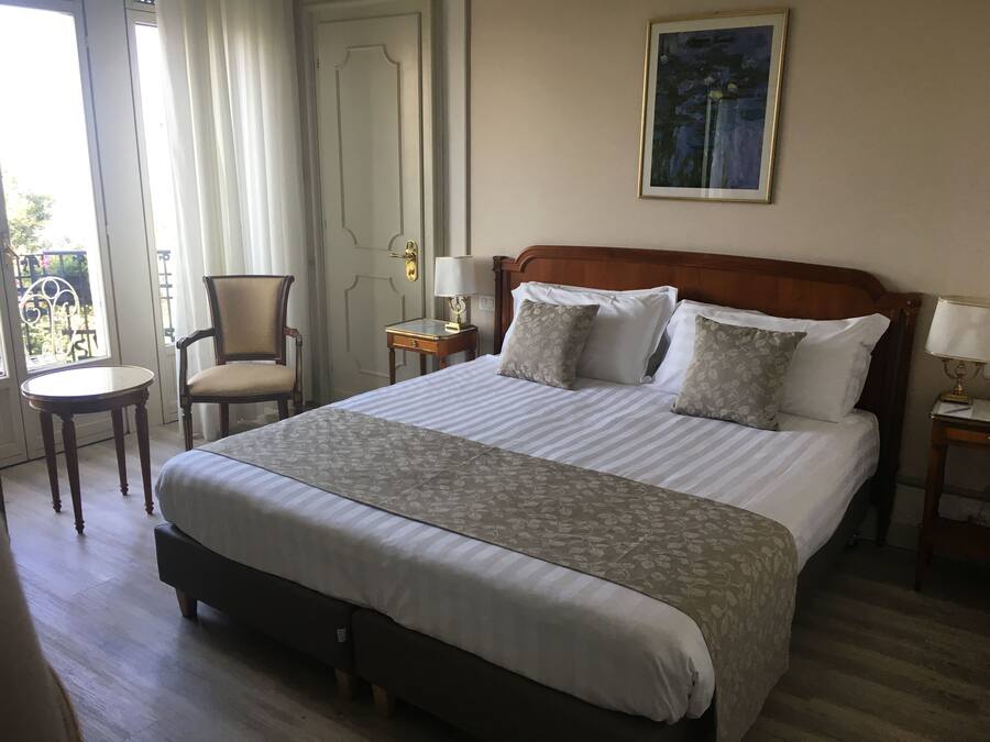 Una habitación de hotel con una cama grande, una silla, una mesita y un cuadro en la pared.