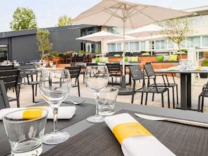 Un área de comedor al aire libre con mesas, sillas y sombrillas.
