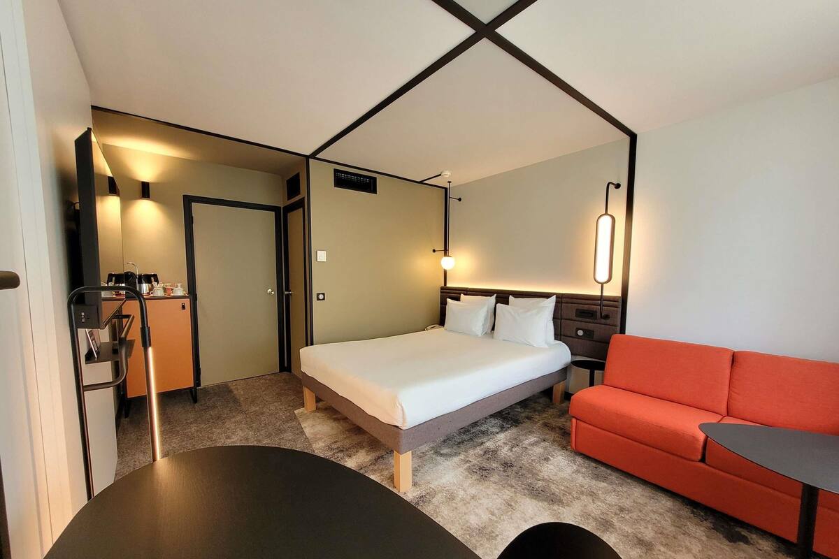 Una habitación de hotel con cama, escritorio, sofá rojo y una mesita.