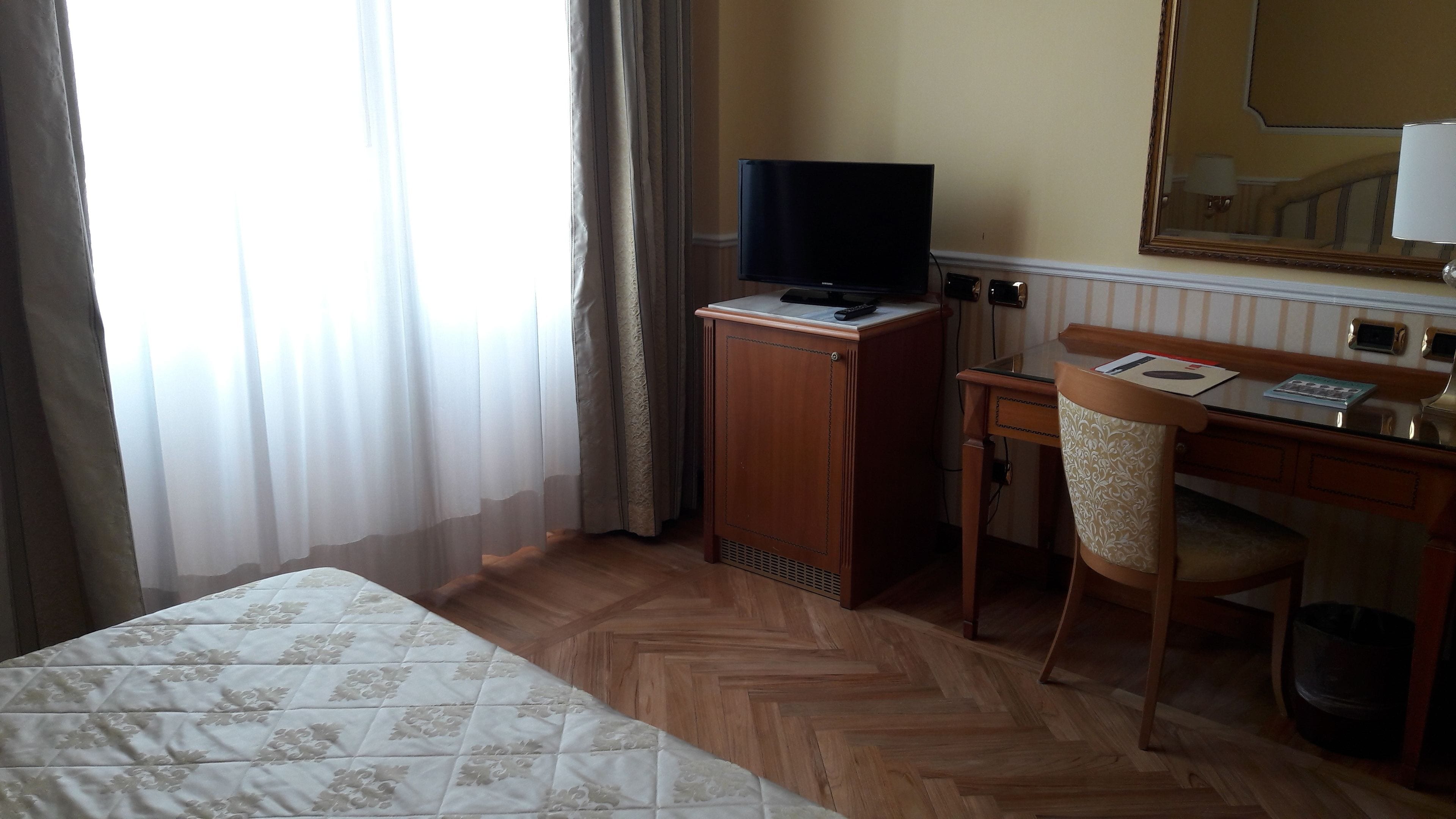 A hotel room with a bed, a desk with a chair, a television, and a mirror.