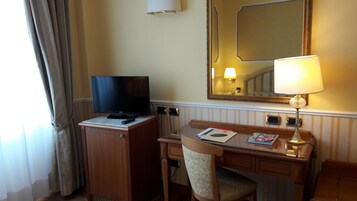 A hotel room with a wooden desk, a television, a lamp, and a chair.