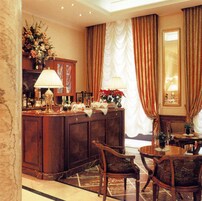Una hall d'albergo con una colonna in marmo, una reception, un'area ristorazione con un tavolo e sedie, e un'ampia finestra con tende.