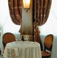 Een eettafel met een witte tafelkleed, twee stoelen en drie wijnglazen.