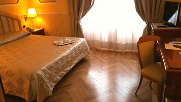 A hotel room with a large bed, a desk with a computer, and a chair.