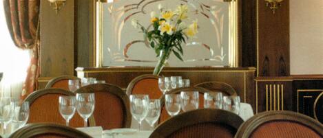 Una mesa de comedor con sillas, un florero con flores y apliques de pared.