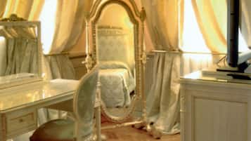 Una camera da letto con un grande specchio decorato, una toeletta con specchio, una televisione su un mobile e un letto con testiera.