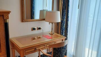 A room with a wooden desk, a chair, a mirror, a lamp, and a window with curtains.